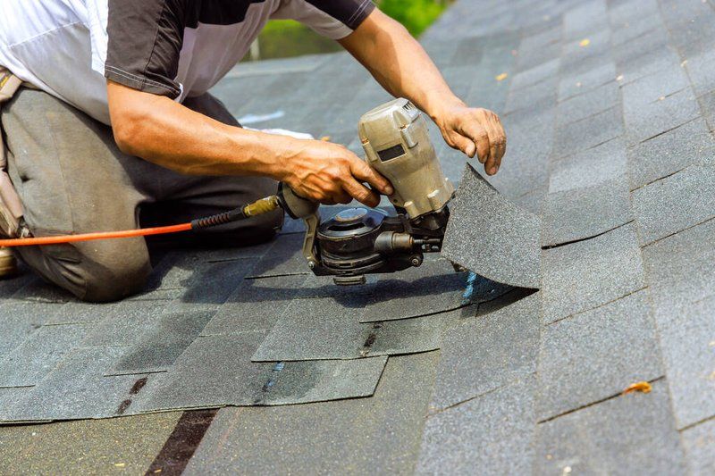 Emergency storm damage repair underway on a residential roof after high winds lifted shingles